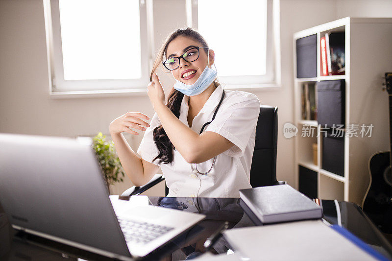 Portrait of young female doctor putting on a protective mask for coronavirus during video call with patient